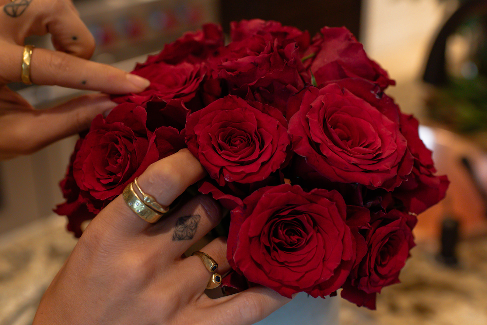 Hands with gold rings tending a bouquet of deep red roses